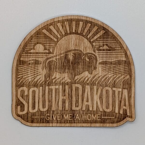 Wood sticker showing a buffalow with a sun filled praire vista with South Dakota give me a home text