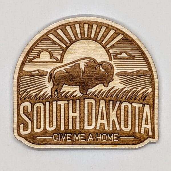 Wood magnet showing a buffalow with a sun filled praire vista with South Dakota give me a home text