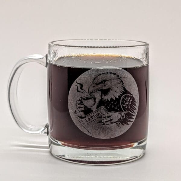 Glass coffee mug engraved with an eagle reading a newspaper and drinking coffee